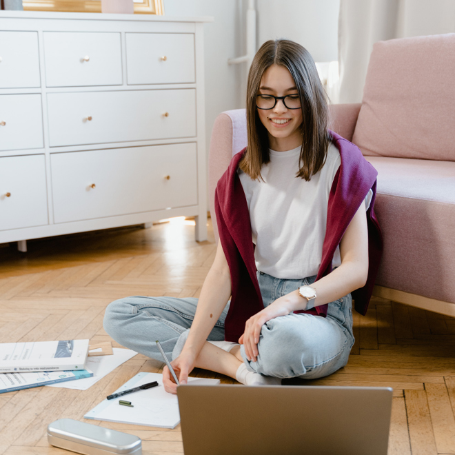 female student sitting on floor with laptop and papers